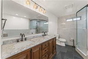 Bathroom featuring dual vanity, a textured ceiling, walk in shower, toilet, and tile floors