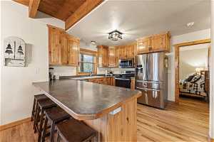 Kitchen featuring beamed ceiling, appliances with stainless steel finishes, light hardwood / wood-style floors, a breakfast bar area, and kitchen peninsula