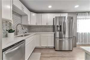 Kitchen featuring appliances with stainless steel finishes, backsplash, light hardwood / wood-style floors, white cabinetry, and sink