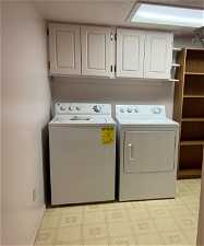 Washroom featuring cabinets, washing machine and dryer, and light tile floors