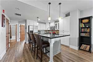 Kitchen featuring decorative light fixtures, appliances with stainless steel finishes, light hardwood / wood-style flooring, a kitchen island with sink, and white cabinetry