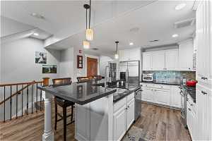 Kitchen with a kitchen bar, stainless steel appliances, a kitchen island with sink, pendant lighting, and light wood-type flooring
