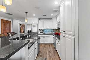 Kitchen with hanging light fixtures, stainless steel appliances, light hardwood / wood-style floors, and white cabinetry