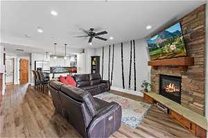 Living room featuring a stone fireplace, ceiling fan, sink, and light wood-type flooring