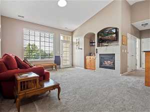 Living room with light carpet, high vaulted ceiling, and a fireplace