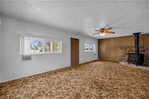 Unfurnished living room featuring carpet flooring, ceiling fan, a textured ceiling, and a wood stove