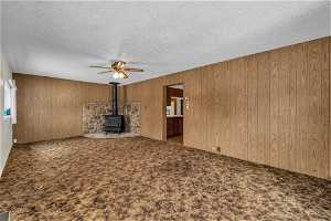 Unfurnished living room with a wood stove, a textured ceiling, carpet floors, and wood walls