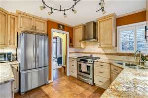Kitchen with backsplash, wall chimney range hood, stainless steel appliances, sink, and light stone counters