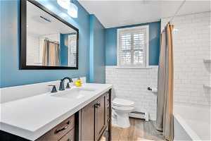Full bathroom with shower / bath combination with curtain, vanity, tile walls, hardwood / wood-style flooring, and toilet