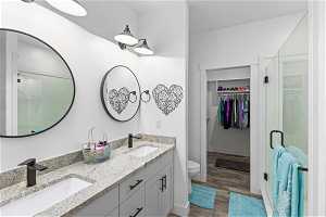 Bathroom with hardwood / wood-style floors, a shower with shower door, toilet, and dual vanity