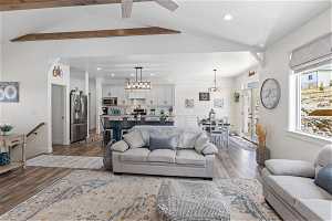 Living room with vaulted ceiling with beams, light hardwood / wood-style floors, and ceiling fan