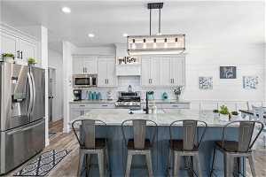 Kitchen featuring white cabinets, hanging light fixtures, dark hardwood / wood-style flooring, stainless steel appliances, and a center island with sink