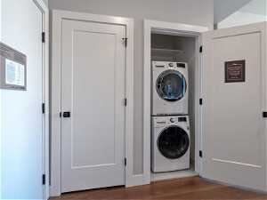 Laundry room with stacked washer and clothes dryer and dark hardwood / wood-style flooring