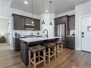 Kitchen with tasteful backsplash, dark wood-type flooring, decorative light fixtures, stainless steel appliances, and a kitchen island with sink