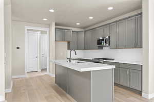 Kitchen featuring appliances with stainless steel finishes, sink, light hardwood / wood-style floors, backsplash, and a center island with sink