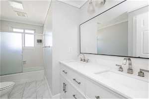 Full bathroom with vanity with extensive cabinet space, double sink, toilet, tile floors, and shower / bath combination with glass door