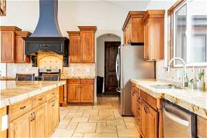 Kitchen featuring premium range hood, range, backsplash, light tile floors, and stainless steel dishwasher