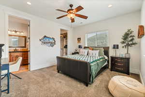 Carpeted bedroom featuring ensuite bathroom, ceiling fan, a closet, sink, and a walk in closet