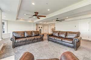Living room with ceiling fan, carpet floors, and a tray ceiling