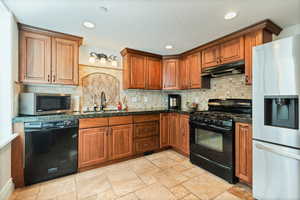 Kitchen with backsplash, light tile floors, black appliances, and sink