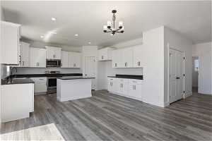Kitchen with appliances with stainless steel finishes, white cabinets, sink, hanging light fixtures, and wood-type flooring