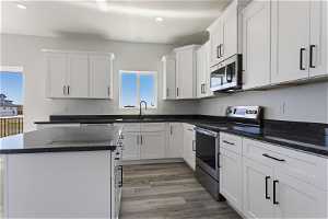Kitchen featuring sink, stainless steel appliances, white cabinetry, hardwood / wood-style floors, and a center island