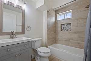 Full bathroom featuring vanity with extensive cabinet space, shower / bathtub combination with curtain, toilet, and tile shower and flooring