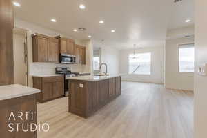 Kitchen featuring appliances with stainless steel finishes, light wood-type flooring, a kitchen island with sink, sink, and hanging light fixtures