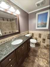 Bathroom featuring tile walls, large vanity, toilet, tile floors, and ornamental molding