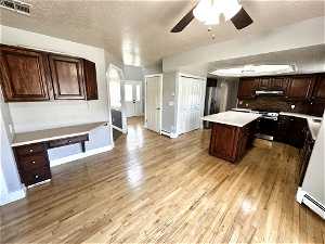 Kitchen with a center island, light hardwood / wood-style floors, dark brown cabinets, and stainless steel range oven