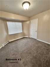 Carpeted empty room featuring a textured ceiling and baseboard heating