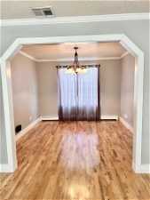 Unfurnished room featuring a chandelier, crown molding, a textured ceiling, and hardwood / wood-style floors
