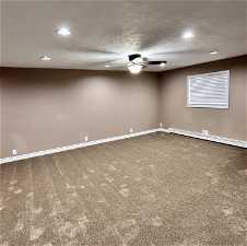 Empty room with carpet flooring, baseboard heating, ceiling fan, and a textured ceiling