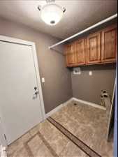 Clothes washing area with hookup for a washing machine, a textured ceiling, cabinets, and light tile floors
