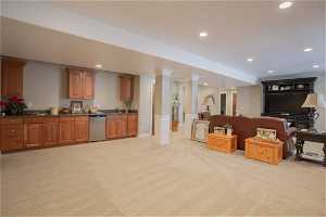 Kitchen with stainless steel dishwasher, light colored carpet, ornate columns, and sink