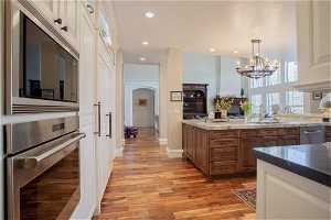 Kitchen featuring light stone countertops, appliances with stainless steel finishes, light hardwood / wood-style flooring, sink, and pendant lighting
