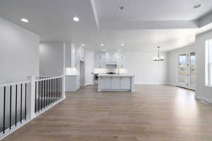 Interior space featuring light hardwood / wood-style flooring, a notable chandelier, a center island with sink, white cabinets, and pendant lighting