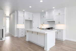 Kitchen featuring an island with sink, sink, white cabinets, and light wood-type flooring