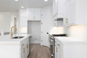 Kitchen featuring a center island with sink, hardwood / wood-style flooring, white cabinets, sink, and appliances with stainless steel finishes