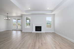 Unfurnished living room featuring a chandelier, light hardwood / wood-style flooring, and a tray ceiling