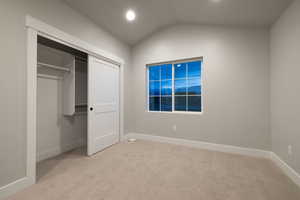 Unfurnished bedroom featuring vaulted ceiling, light carpet, and a closet