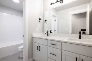 Full bathroom featuring dual vanity, tile floors, toilet, and shower / bathtub combination