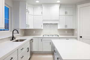 Kitchen with backsplash, sink, white cabinetry, and light hardwood / wood-style floors