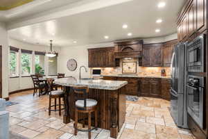 Kitchen with appliances with stainless steel finishes, light tile floors, backsplash, hanging light fixtures, and a center island with sink