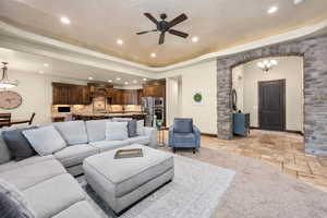 Living room featuring ceiling fan with notable chandelier, a tray ceiling, and light tile floors