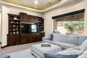 Carpeted living room with ceiling fan and a raised ceiling