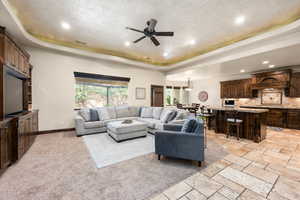 Carpeted living room with a textured ceiling, ceiling fan, and a raised ceiling