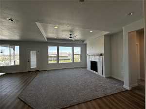Unfurnished living room with a fireplace, dark colored carpet, ceiling fan, and a textured ceiling