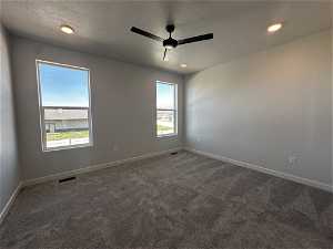 Empty room with ceiling fan, carpet floors, and a textured ceiling