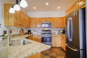 Kitchen featuring dark tile floors, tasteful backsplash, stainless steel refrigerator, sink, and range with gas cooktop